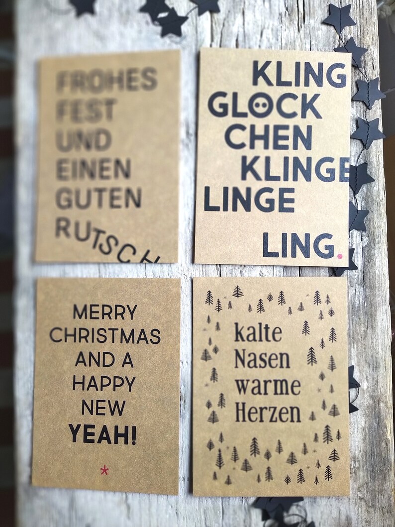 May include: Four brown cards with black text. The first card says "Frohes Fest und einen guten Rutsch". The second card says "Kling Glock Chen Klinge Linge Ling". The third card says "Merry Christmas and a Happy New Yeah!". The fourth card says "Kalte Nasen Warme Herzen" and has a pattern of small pine trees.