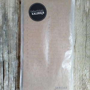 May include: A brown paper calendar with a black circle sticker that says "Geburtstags-KALENDER" and the month "JANUAR" printed at the bottom. The calendar has numbered days from 1 to 31.