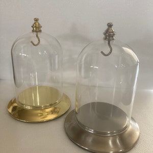 May include: Two glass display domes with gold and silver bases. Each dome has a hook on the top.
