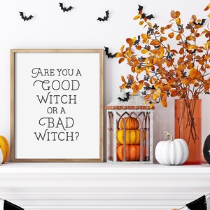 May include: A white mantelpiece with a framed print that reads "Are you a good witch or a bad witch?"  There are pumpkins, a lantern with pumpkins inside, a vase with fall foliage, and a black pumpkin with the word "boo!" written on it.  There are black bats on the wall behind the mantelpiece.