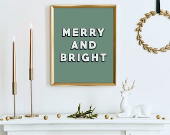 May include: A gold framed print with a green background and the text "Merry and Bright" in white letters with a navy blue outline. The print is on a white mantel with two gold candlesticks, a white deer figurine, and gold ornaments.