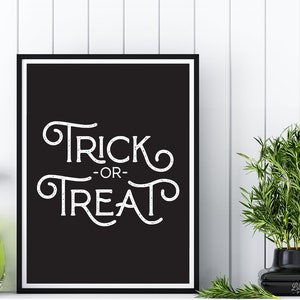 May include: Black and white printable sign with the text "Trick or Treat" in a decorative font. The sign is framed in a black frame and is hanging on a white wall.