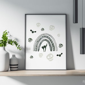 May include: A framed print featuring a Halloween-themed design. The artwork showcases a black cat under a gray and white rainbow, surrounded by skulls and bats. The print is displayed on a wooden shelf with white vases and greenery.