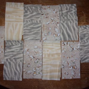 May include: A collection of 10 fabric squares with a beach theme. The squares feature a variety of patterns, including seashells, sand, and waves. The fabric is a light beige color with brown and white accents.