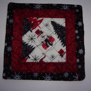 May include: A red, black, and white quilted square with a snowman and Christmas trees design. The fabric has a quilted texture and a snowflake border.