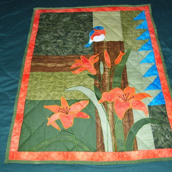 Blue birds and daylilies machine quilted wall quilt. The blue bird is sitting on a fence post looking pretty.