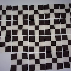 May include: A collection of 36 black and white checkered fabric squares. The squares are arranged in a grid pattern.