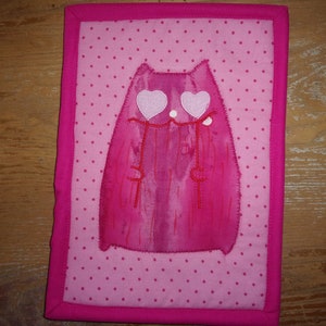 May include: Pink fabric cat with white heart eyes on a pink polka dot background.