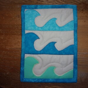 May include: A blue and white quilted wall hanging with a design of three waves. The waves are outlined in white and the background is a sparkly white fabric.