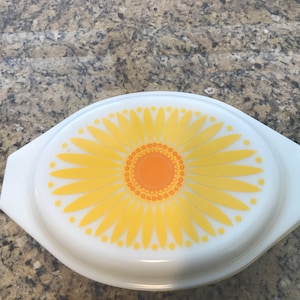 May include: White oval baking dish with a yellow and orange sunflower design. The sunflower has a yellow center with orange petals and a white background.