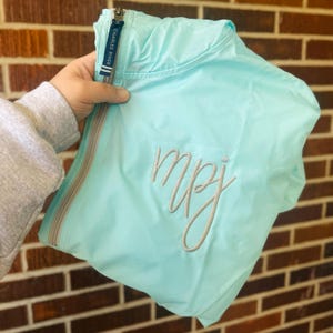 May include: A light blue hooded jacket with a zipper closure and a silver embroidered monogram "mpj".