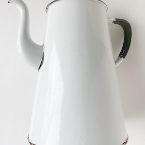 Puede incluir: Cafetera de esmalte blanco con asa negra. La cafetera tiene un pico y un cuerpo redondeado.