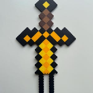 May include: A black, yellow and brown Minecraft sword made of perler beads.