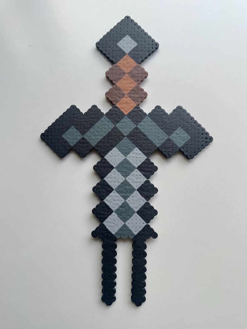 May include: A black, grey and brown pixelated sword made of beads. The sword has a diamond-shaped blade and a handle with a chequered pattern.