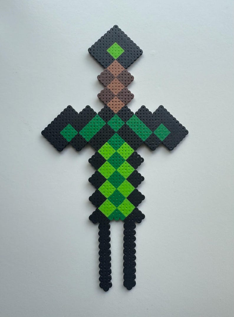 May include: A green and black pixelated sword made of plastic beads. The sword has a brown handle and a green blade.