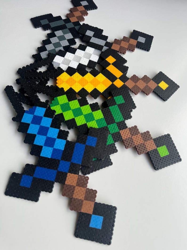 May include: Six different coloured Minecraft swords made of perler beads. The swords are arranged in a stack, with the blue sword at the bottom and the grey sword at the top. The swords are all the same size and shape, and they have a black handle and a diamond-shaped blade.
