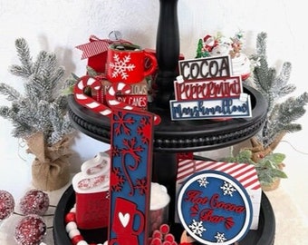 May include: A three-tiered black tiered tray decorated with red and white Christmas decorations. The top tier features a snowman figurine, a red mug, and a white and red wooden mug. The middle tier features a red mug, a candy cane, and a wooden sign that says "Cocoa Peppermint Marshmallows". The bottom tier features a red and white striped box, a red and white wooden sign that says "Hot Cocoa Bar", and a red and white wooden sign that says "Merry Christmas".