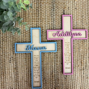 May include: Two wooden crosses with a blue and pink border. The crosses have the names "Mason" and "Addilynn" on them. The crosses have a prayer inscribed on them that reads "Now I lay me down to sleep, I pray the Lord my soul to keep. Angels watch me through the night, and wake me with the morning light. Amen."
