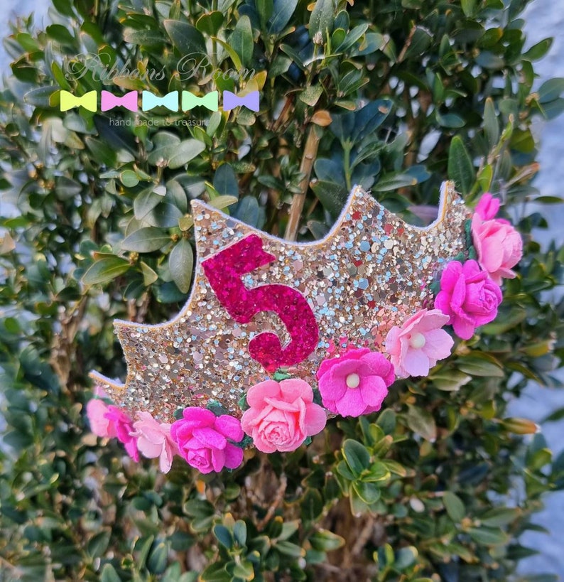 May include: Gold glitter crown with a pink felt number 5 and pink felt flowers. The crown is decorated with gold glitter and pink felt flowers.