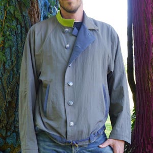 May include: A gray jacket with a lime green collar and blue accents. The jacket has a button-up front and two pockets. The model is wearing blue jeans. The text "DongoDesign" is visible on the lower right.