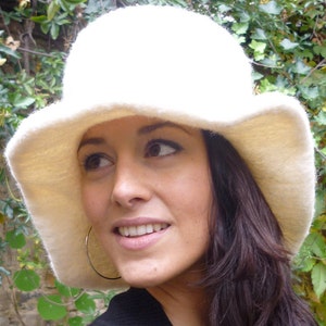 Può includere: Un cappello color crema a tesa larga con un aspetto morbido e strutturato. Il cappello ha una corona arrotondata e una tesa dolcemente inclinata. L'immagine include anche il testo "DongoDesign" nell'angolo in basso a destra.