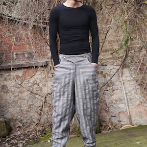 May include: A person wearing a black long-sleeved shirt and striped pants. The pants have a unique design with a diagonal seam and a wide leg.