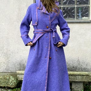 May include: A long purple wool coat with a matching purple hat. The coat has a belt and a double breasted closure. The coat is lined with a red and orange trim.