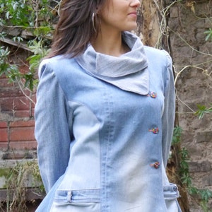 May include: A light blue denim jacket with a gray cowl neck and colorful buttons. The jacket has a slightly flared hem and a patch pocket on the front. The text "DongoDesign" is visible in the bottom right corner of the image.