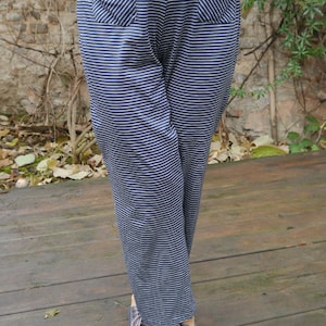 May include: A pair of striped pants with two pockets in the front. The pants are a dark blue color with white stripes. The person is wearing gray shoes with pink laces.
