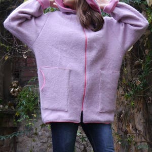 May include: A light purple hooded jacket with a pink interior and trim. The jacket has two large front pockets and a full-length zipper. The model is wearing blue jeans. The text "DongoDesign" is visible at the bottom right.