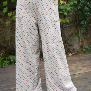 May include: Wide-leg trousers with a white background and a small, colourful teardrop pattern. The trousers have a high waist and pockets on the sides.