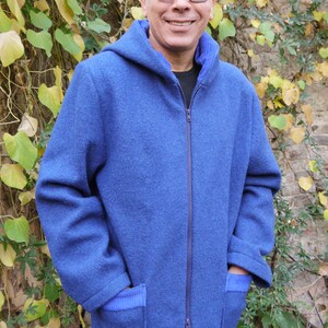Può includere: Una giacca blu con cappuccio, chiusura a zip e due tasche. La giacca ha un bordo a costine intorno al cappuccio e alle tasche.