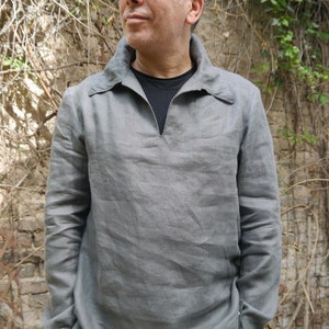 Puede incluir: Una camisa de lino gris con cuello en V y mangas largas. La camisa tiene un cuello que se pliega hacia abajo y un cierre de botón en el cuello. La camisa está hecha de una tela suave y cómoda y tiene un ajuste holgado.