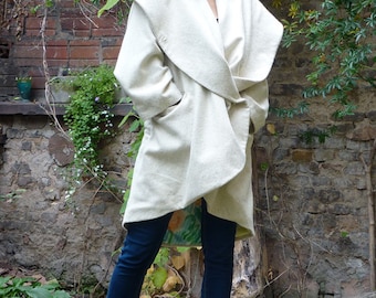 May include: A white wrap coat with a large collar and a tie belt. The coat is made of a soft, textured fabric. The model is wearing blue jeans and beige shoes.