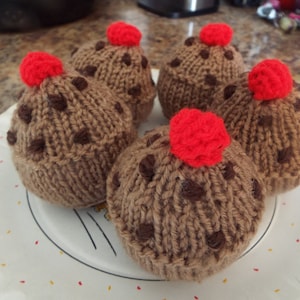 Puede incluir: Cinco cupcakes de punto sobre un plato. Los cupcakes son marrones con detalles de chispas de chocolate marrón oscuro y una cereza roja encima. El plato es blanco con un diseño negro simple.