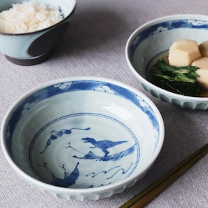 May include: A collection of Japanese-style ceramic bowls. The bowls feature blue and white designs, including a dinosaur motif. One bowl contains rice, while another holds food. Chopsticks are placed in the foreground.