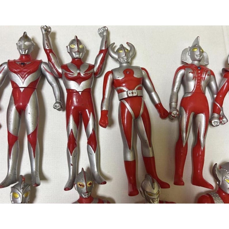 May include: A collection of Ultraman action figures featuring red and silver color schemes. The figures display various poses, including arms raised and standing positions, with distinct head designs, including one with prominent horns.