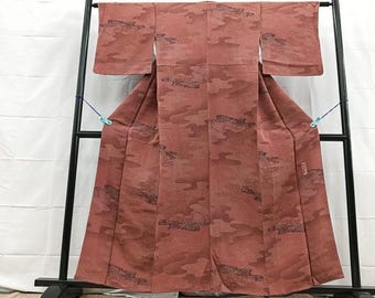 Könnte beinhalten: Ein rotbrauner Kimono mit wolkenartigem Muster und schwarzen Akzenten, ausgestellt auf einem schwarzen Metallgestell. Das traditionelle japanische Kleidungsstück hat lange Ärmel und ein fließendes Design. Der Stoff hat ein strukturiertes Aussehen, und das Kleidungsstück ist vollständig sichtbar.