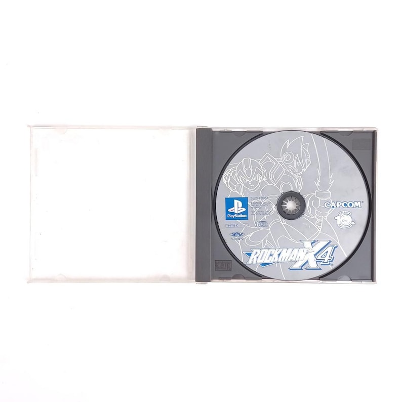 Puede incluir: Un disco de juego de PlayStation plateado con una ilustraci&oacute;n en blanco y negro de personajes del videojuego Rockman X4. El disco tiene el texto "Rockman X4" y "CAPCOM" impreso en &eacute;l.