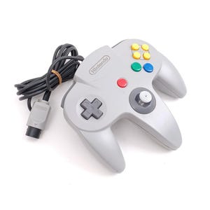 May include: A gray Nintendo 64 controller with a black cord and a gray plug. The controller has a red button, a gray joystick, and a set of colored buttons.