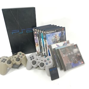 May include: A black PlayStation 2 console with the logo "ps2" in blue, accompanied by two controllers, game discs, and a memory card. The game cases are labeled "PlayStation 2" and "Gundam".