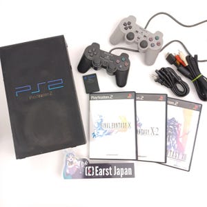 May include: A black PlayStation 2 console with two controllers, memory card, and three Final Fantasy game cases. Cables and connectors are also included. The console has the text "PS2 PlayStation 2" on the front.