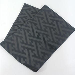 May include: Two dark gray fabric pieces with a repeating geometric pattern. The pattern consists of interlocking shapes in a slightly lighter shade of gray. The fabric is folded and appears to be a textile, possibly for home decor or apparel.