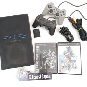 May include: A black PlayStation 2 console with two controllers, memory card, and two game cases. The game cases are labeled "Kingdom Hearts" and "Kingdom Hearts II". The console has the text "PS2 PlayStation 2" on the front.