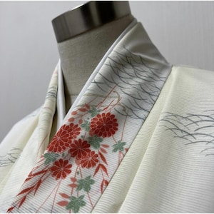 May include: Cream-colored kimono with a floral pattern. The kimono features a decorative border with red chrysanthemum flowers, green leaves, and gray wave-like designs. The fabric has a subtle ribbed texture.
