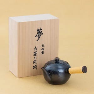 May include: A black Japanese teapot with a light-colored bamboo handle and a matching lid. The teapot is next to a wooden box with Japanese characters. The box is light brown.