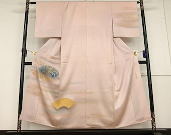 Könnte beinhalten: Ein hellrosa Kimono mit einem dezenten Karomuster, der auf einem schwarzen Gestell präsentiert wird. Der Kimono hat ein Design aus einem Fächer und einem blau-goldenen Design. Das Kleidungsstück ist aus einem weichen, fließenden Stoff gefertigt.