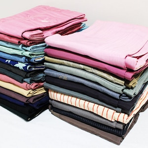 Op de afbeelding: Een stapel gevouwen kleding in verschillende kleuren en patronen, waaronder roze, blauw, groen en bruin. De kleding is netjes in een stapel geordend.