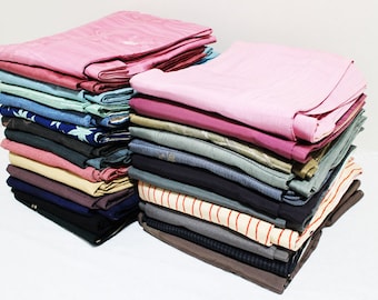 Puede incluir: Una pila de ropa doblada en varios colores y patrones, incluyendo rosa, azul, verde y beige. La ropa está ordenada cuidadosamente en una pila, con la capa superior doblada.