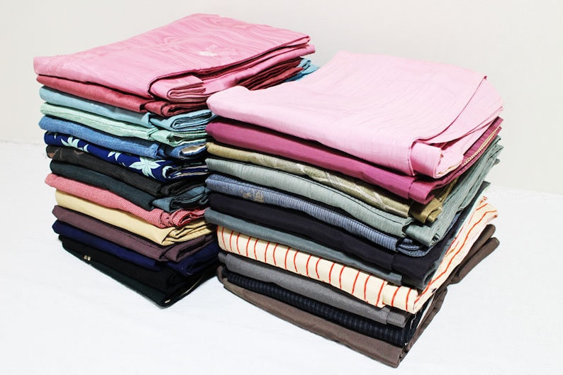 Op de afbeelding: Een stapel gevouwen kleding in verschillende kleuren en patronen, waaronder roze, blauw, groen en bruin. De kleding is netjes in een stapel geordend.